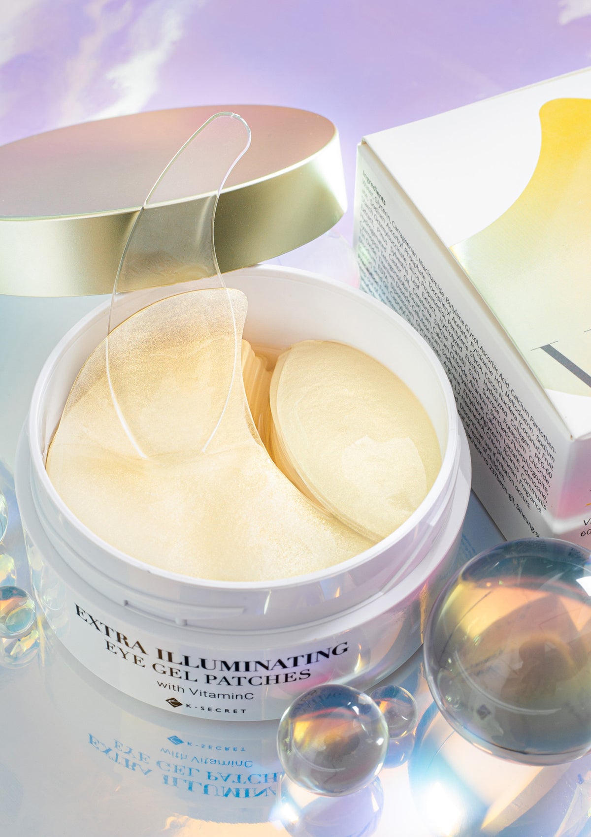 A box of K-Secret Extra Illuminating Eye Gel Patches with Vitamin C, showing the product name and patches in yellow color with a golden spatula.